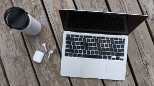 A laptop open on an outdoor deck, with headphones and a water bottle