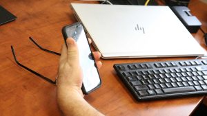 Photo of a desk with a laptop and a hand holding a mobile phone