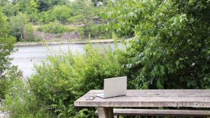 A laptop on a wooden table with a river landscape in the background