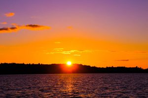 Sunset on a lake with the sun disappearing behind the trees on the far shore