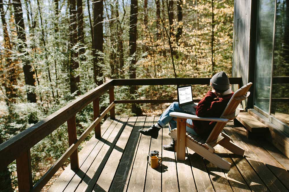 A woman sits on an outdoor deck and works on a laptop