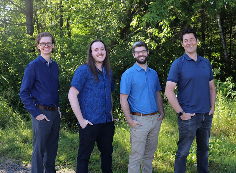 The Lakeland Networks IT Team, four men in blue shirts, stands in front of a forest background.