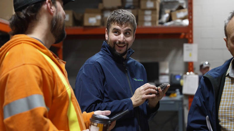 A smiling Lakeland employee in a blue jacket speaks to another employee wearing an orange hoodie with reflective safety stripes.