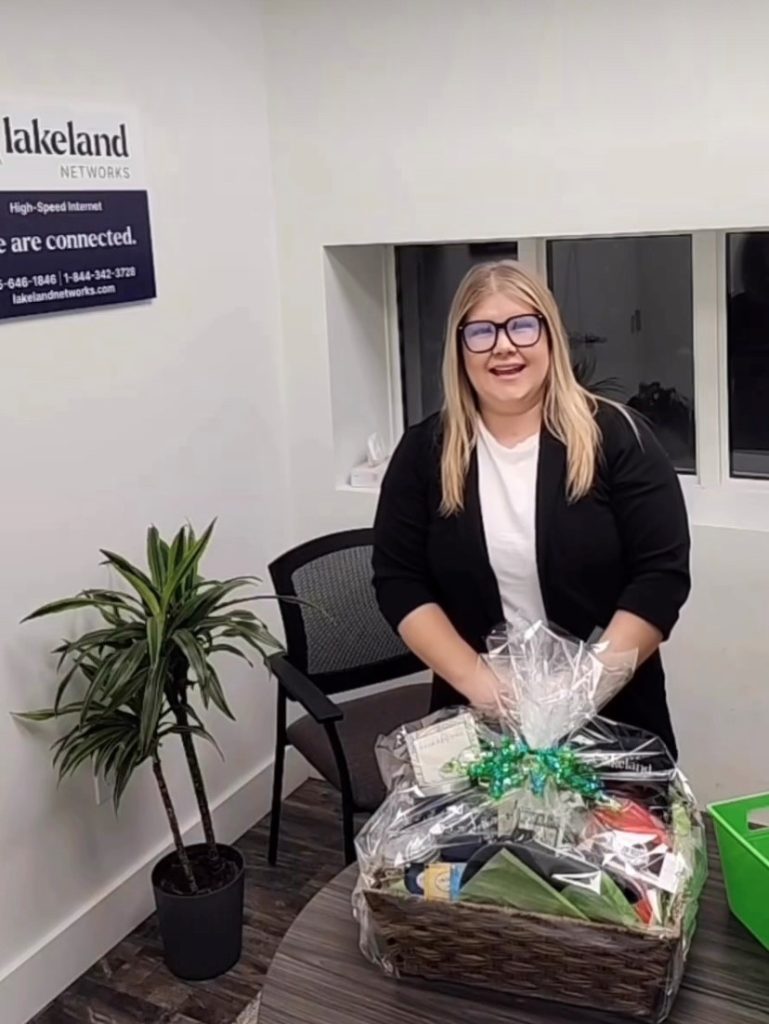 Our customer representative, Jo standing behind a giveaway basket with a lakeland networks sign behind her.