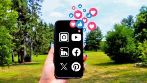 hand holding phone in the air with social media icons on it. There are hearts and thumbs up icons emanating from the phone