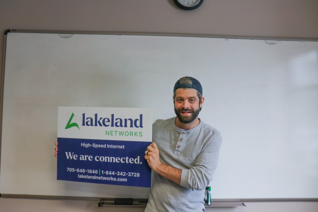 Lakeland Networks team member holding up a lawn sign with business information on it.