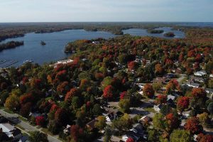 Drone image of Muskoka neighbourhood among colour changing trees in the fall with a lake in the distance